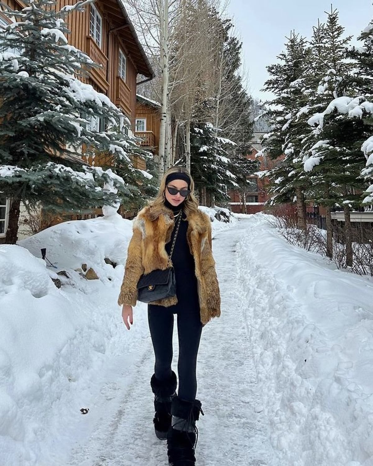 Aspen Après-Ski outfit — black knit headband, black slim rectangular sunglasses, tan and brown fox-fur jacket, black fitted turtleneck top, black quilted Chanel flap bag
