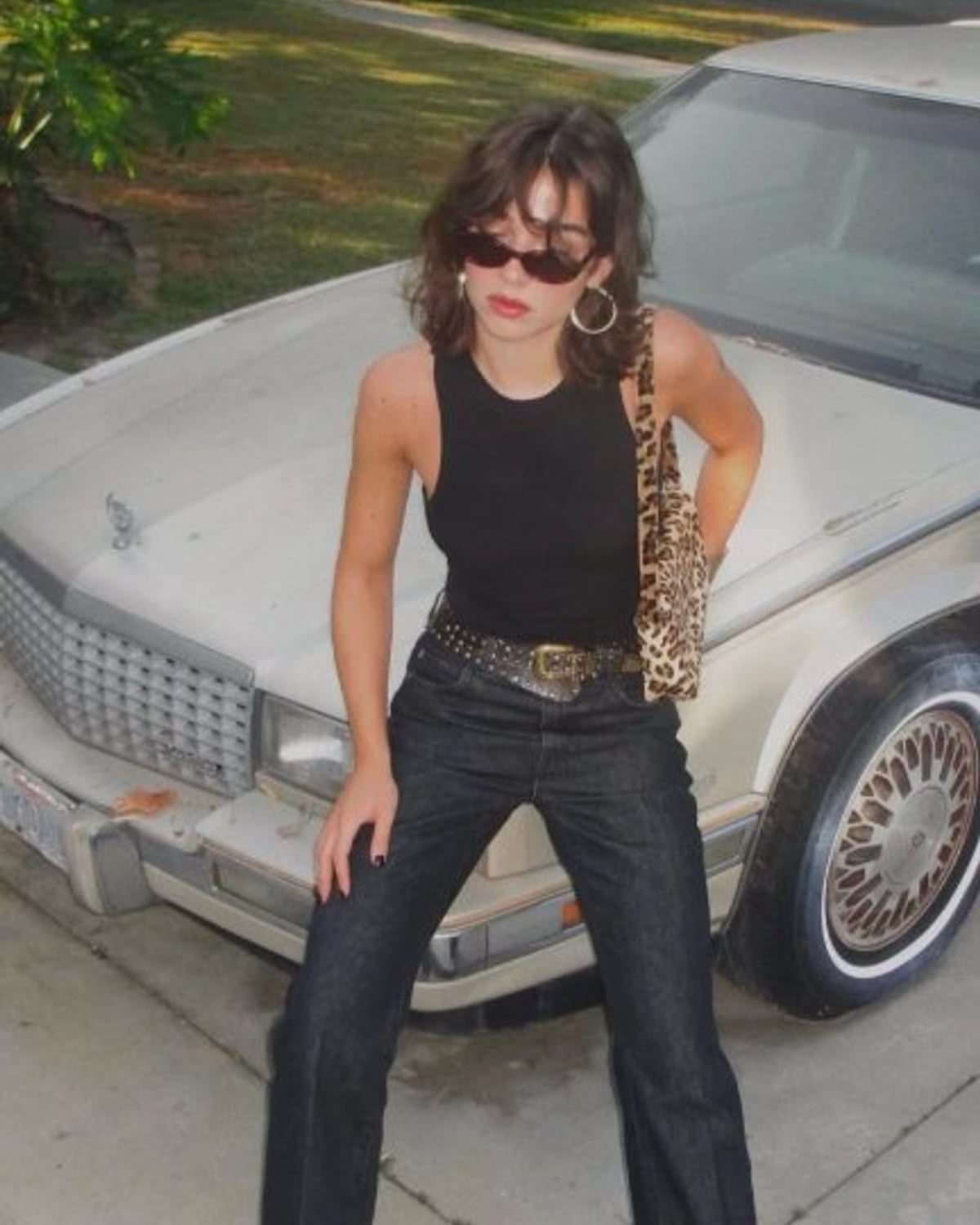 Mob Wife outfit — black ribbed tank top, dark bootcut jeans, studded leather belt with ornate buckle, pointed-toe oxblood ankle boots, leopard-print shoulder bag