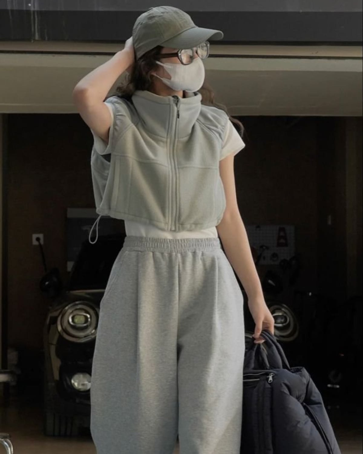 Seoul Soft-Tech outfit — sage green nylon baseball cap, oversized round clear-frame glasses, cropped sage short-sleeve zip-up vest, white ribbed cropped tee, heather grey wide-leg sweatpants