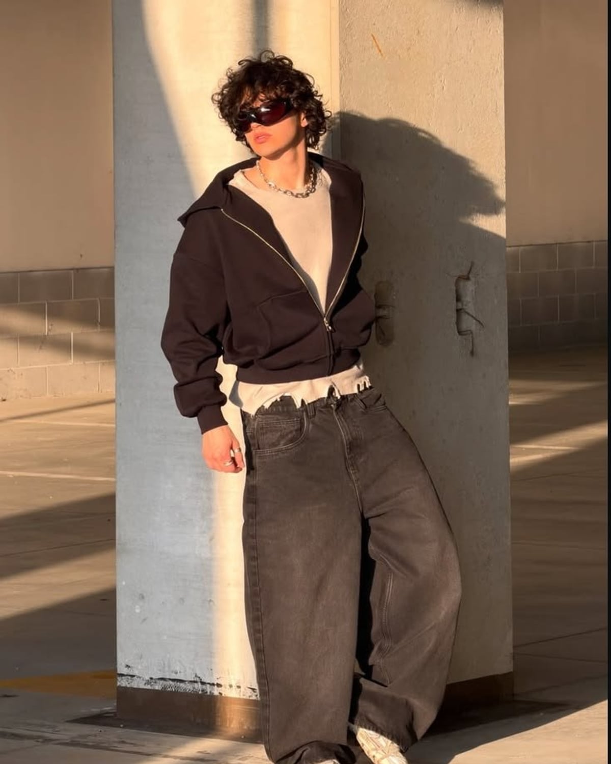 Streetwear outfit — wraparound shield sunglasses, chunky silver curb-link chain necklace, men's cream cotton t-shirt, men's dark brown oversized zip-up hoodie, men's baggy washed black wide-leg jeans